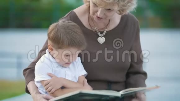 男孩和奶奶在长凳上的公园里看书视频的预览图