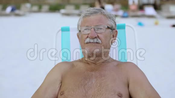 特写一幅留着小胡子的老人的肖像在沙滩躺椅上看着摄像机视频的预览图