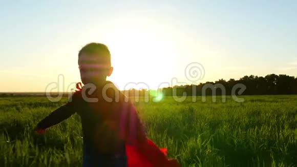 一个穿着超级英雄服装的孩子穿着红色斗篷在夕阳的映衬下穿过绿色的草坪走向视频的预览图