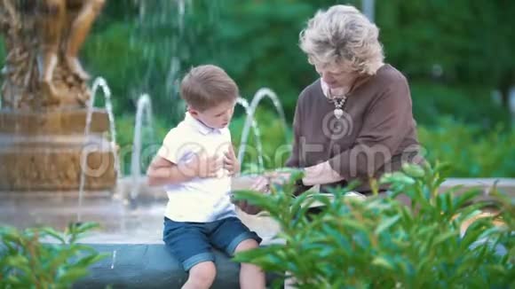 小男孩和奶奶坐在公园的喷泉旁视频的预览图
