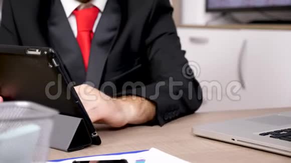 在平板电脑的秘密上用黑色西装和红领带紧紧抓住男人的双手视频的预览图