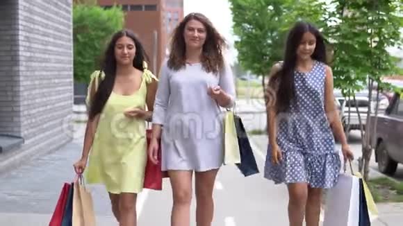 三个漂亮的女朋友购物后带着包裹沿着街走慢动作高清高清视频的预览图