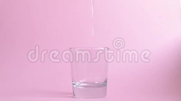 水倒在粉红色背景上的玻璃杯里视频的预览图