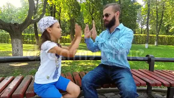 一个爸爸和他的女儿坐在公园的长凳上和她玩视频的预览图