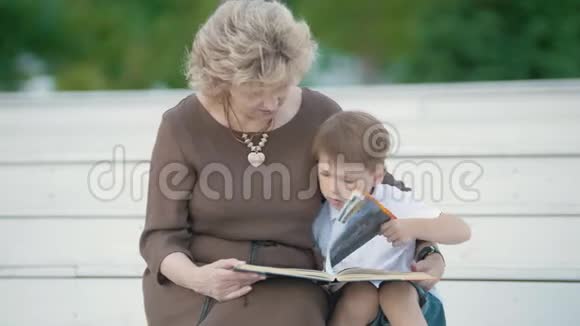 一个男孩和他的祖母在公园里看书坐在白色的台阶上视频的预览图