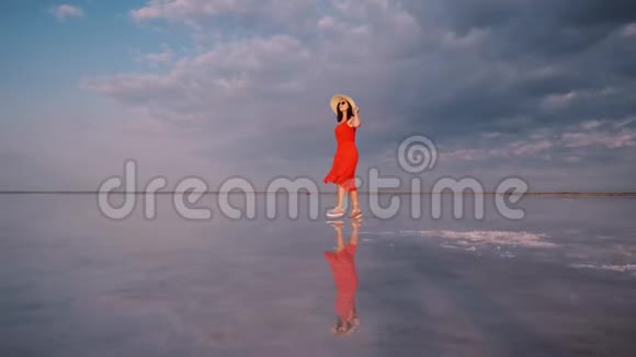 穿着飘舞裙的女孩走在粉红色的盐湖边那里的天空被反射视频的预览图