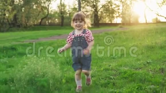 阳光明媚的夏日日落时分快乐的小女孩在绿草上奔跑视频的预览图