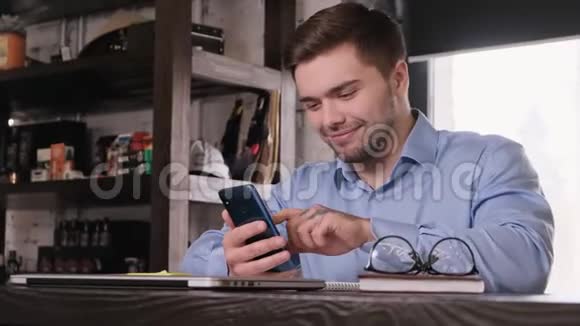 年轻迷人的留胡子商人穿着蓝色衬衫使用智能手机下班休息满意的经理视频的预览图