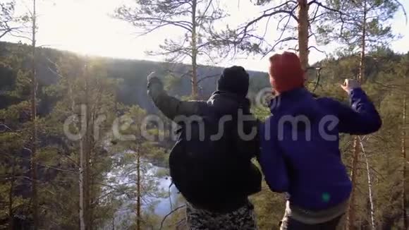 秋天一对幸福的夫妇在一座岩石山上看着日落时峡谷里的河流和针叶林视频的预览图