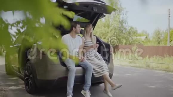 年轻夫妇坐在电动车的后备箱里放松视频的预览图