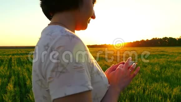 一个女孩手拿着智能手机在夕阳背景下的绿色草坪上慢动作视频的预览图