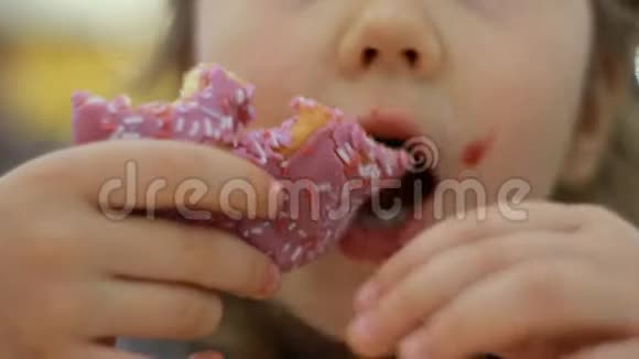小孩嘴咬玫瑰甜甜圈特写小女孩吃甜甜圈加糖美味的甜的甜的视频的预览图