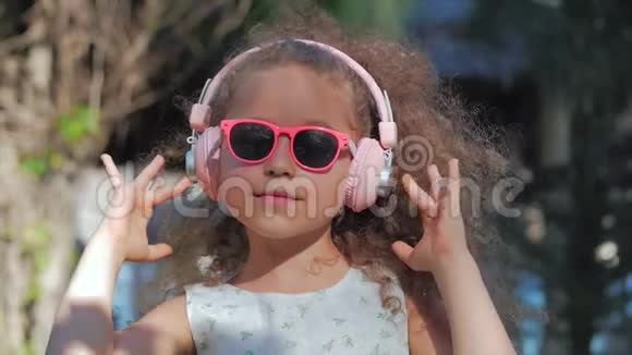 一个可爱的孩子的肖像一个漂亮的小女孩穿着一件白色连衣裙戴着粉红色的眼镜和粉红色的耳机视频的预览图
