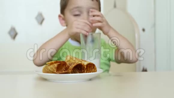 一个快乐的孩子通过吸管喝牛奶吃华夫饼管道坐在桌子旁视频的预览图