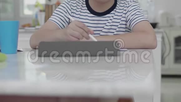 亚洲男孩坐在家里的椅子上用平板电脑做作业找出答案视频的预览图