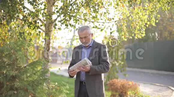 英俊的老人手里拿着报纸穿过公园大胡子爷爷一大早就走在视频的预览图