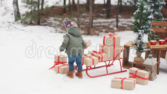 一个小男孩把礼物放在雪橇上概念圣诞快乐围巾和帽子红色的雪橇视频的预览图