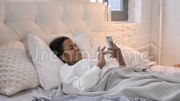 年轻的非洲女孩在床上使用智能手机视频的预览图