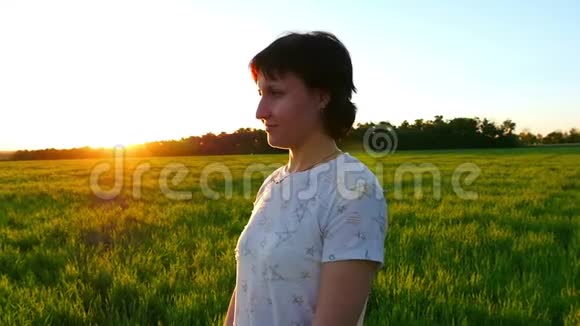 一个年轻女子站在一片绿色的草坪上在日落的背景下缓慢的动作视频的预览图