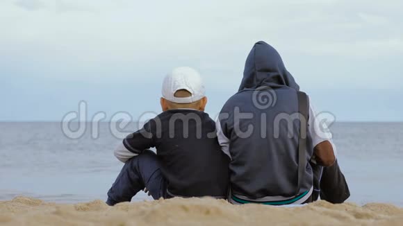 两个男孩坐在海滩上看着大海视频的预览图