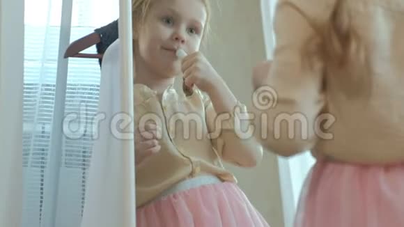 可爱的小女孩一条粉红色的裙子梳着辫子在镜子前涂着口红妈妈视频的预览图