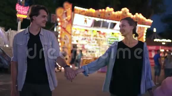 在游乐园里浪漫约会年轻夫妇晚上在游乐场散步女孩手里拿着棉花糖视频的预览图