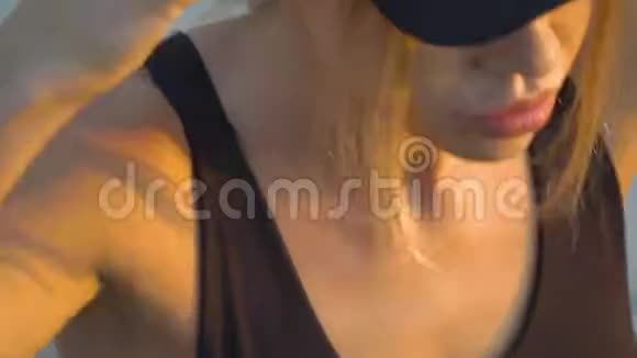 戴着黑帽的金发女郎戴上耳机用智能手表打开音乐视频的预览图