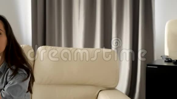 漂亮的女人微笑着自然地对着坐在沙发上的相机视频的预览图