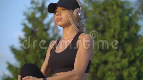 一个戴着耳机手臂上戴着智能手表的女人在公园里热身慢动作视频的预览图