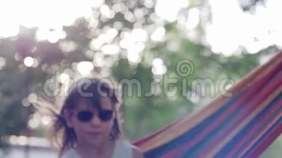 在大自然特写镜头上把小女孩微笑成太阳镜在吊床上摆动视频的预览图