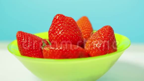 在蓝色背景的绿色碗里放着红色多汁的草莓在一个圆圈里旋转视频的预览图
