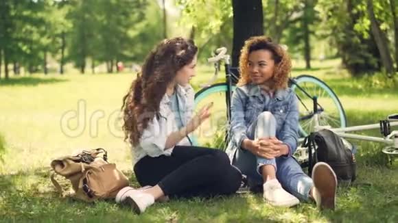 快乐的学生非裔美国人和高加索人骑着自行车坐在公园里谈笑风生视频的预览图