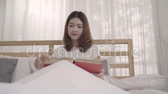 美丽迷人的年轻亚洲女人早上躺在床上放松时在家里的卧室里看书视频的预览图