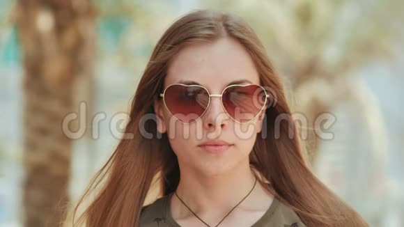 戴太阳镜的女孩在迪拜的街道和棕榈树的背景上面的特写视频的预览图
