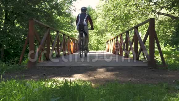 一个人骑自行车穿过公园里的桥慢动作视频的预览图