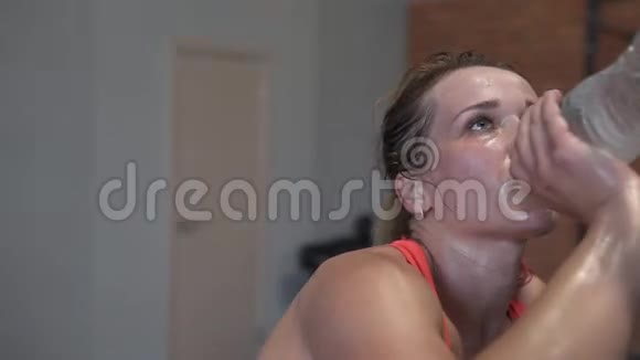 疲惫的汗流浃背的健身妇女在健身房锻炼时喝一瓶水视频的预览图