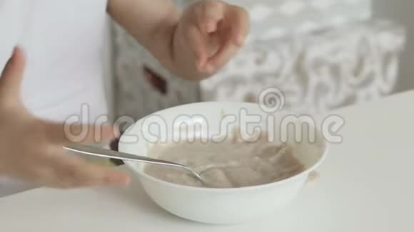 一个小女孩坐在孩子们桌子旁吃盘子里的粥视频的预览图