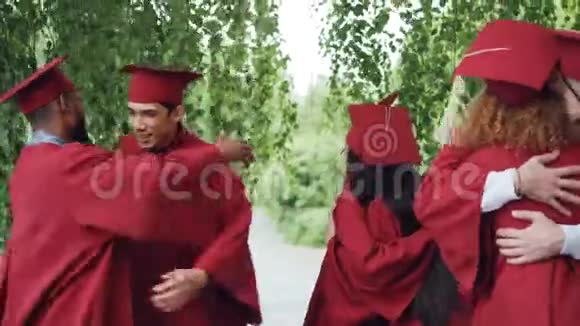 毕业的学生穿着长袍戴着帽子兴奋的年轻人拥抱着互相祝贺笑着视频的预览图