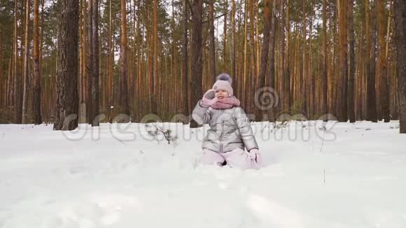 快乐的小女孩用手摇着相机坐在雪地上慢动作视频的预览图