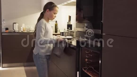 女孩把饼干放在烤箱里在家里的现代厨房里烤视频的预览图
