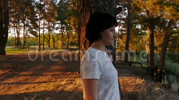 一个年轻的女孩站在河边的悬崖边看着水森林中日落时分一个女人的剪影视频的预览图