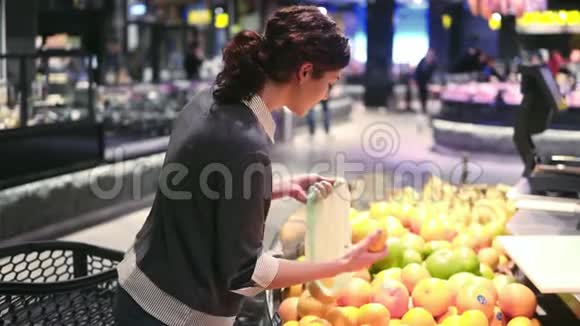 一个20的年轻美丽的黑发女孩在一个水果和蔬菜过道里把橘子放进塑料袋里视频的预览图