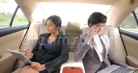 两个年轻的女商人在一辆车的后座上放着平板电脑和笔记本电脑视频的预览图
