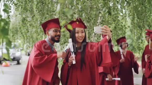 同学们都在自拍带着毕业证书摆着笑脸女孩拿着智能手机人们穿着长袍视频的预览图