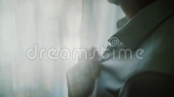 男人把他的白色衬衫扣上纽扣站在明亮的窗户前商业时尚和服装概念接近视频的预览图