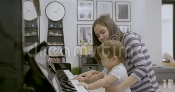 年轻的亚洲妈妈和她的小男孩一起弹钢琴视频的预览图