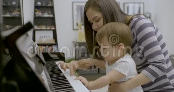 年轻的亚洲妈妈和她的小男孩一起弹钢琴视频的预览图