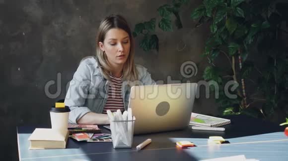 年轻的金发女人坐在办公室里用电脑工作她累了所以她摸了摸她的脸和头发摩擦视频的预览图