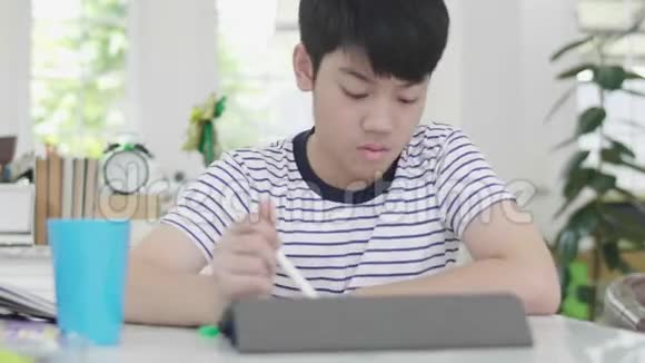 亚洲男孩坐在家里的椅子上做作业用平板电脑找到答案视频的预览图