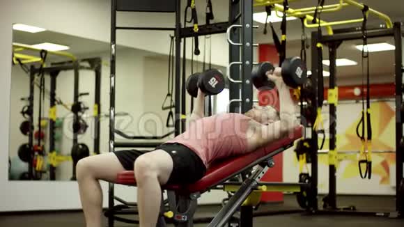 男运动员在健身房的长凳上做哑铃按压练习视频的预览图